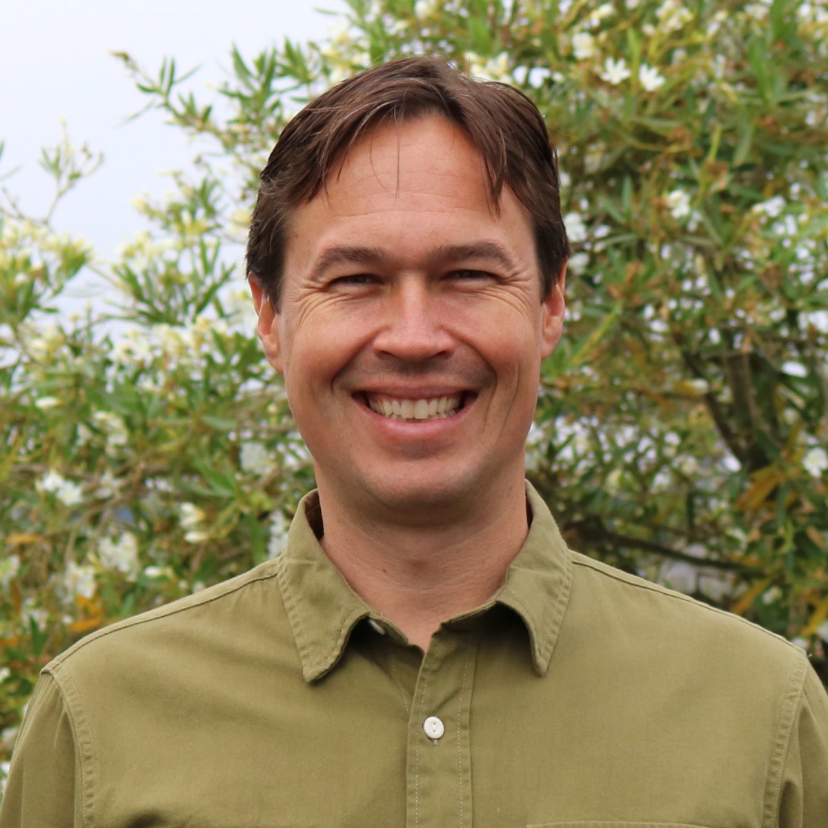 Ben Penning, CEO of Penning Landscapes, smiling outdoors among foliage.