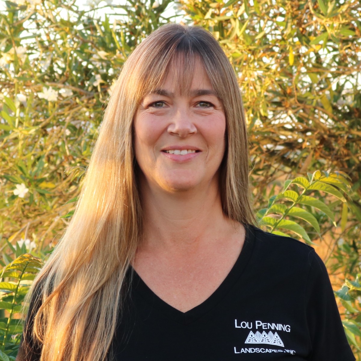 Wendy Jordan, Penning Landscapes office manager, smiling among garden foliage.