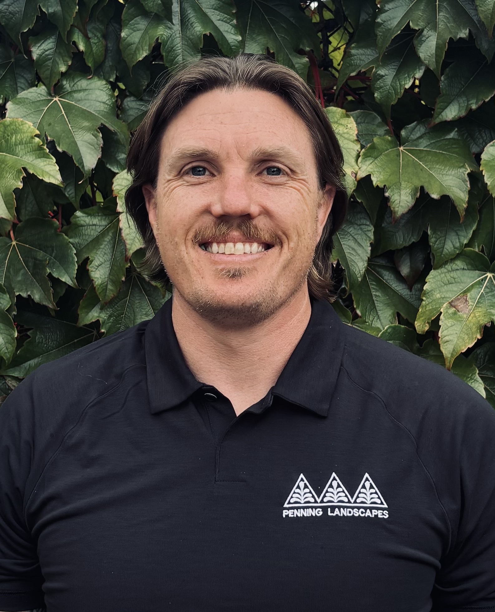 Brandon Augustine, Penning Landscapes maintenance production manager, smiling in front of lush greenery.