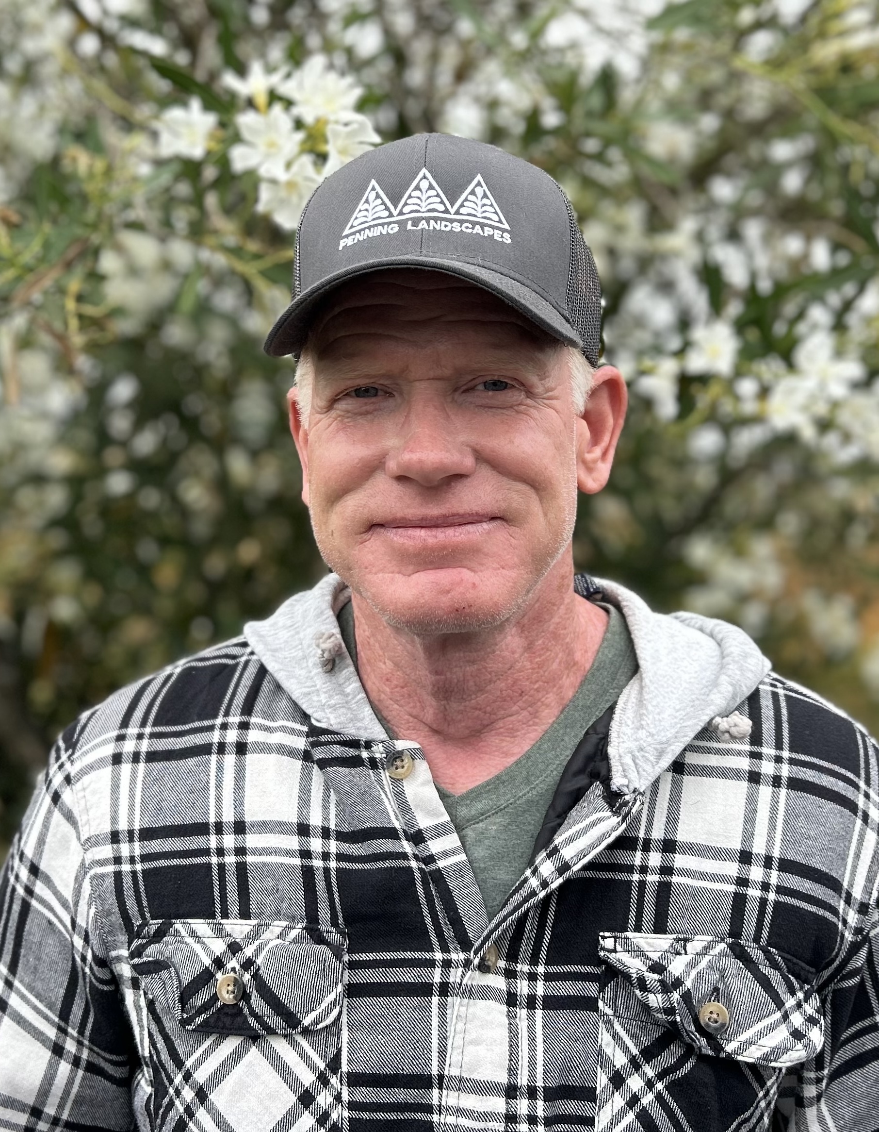 Penning Landscapes team member wearing company hat and plaid shirt, surrounded by blooming fruit trees.