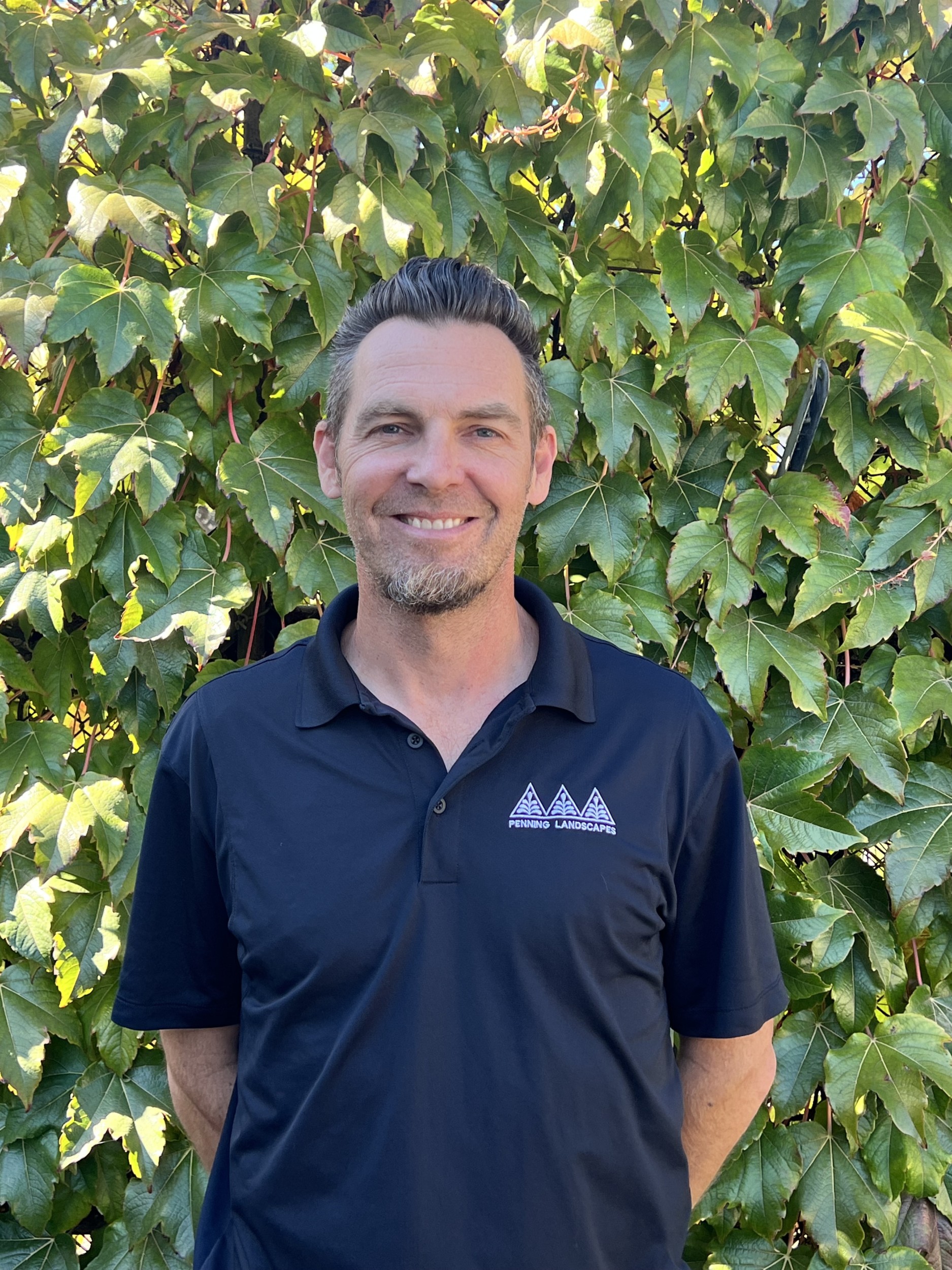 Erick Roldan, Penning Landscapes maintenance account manager, smiling in front of lush foliage.